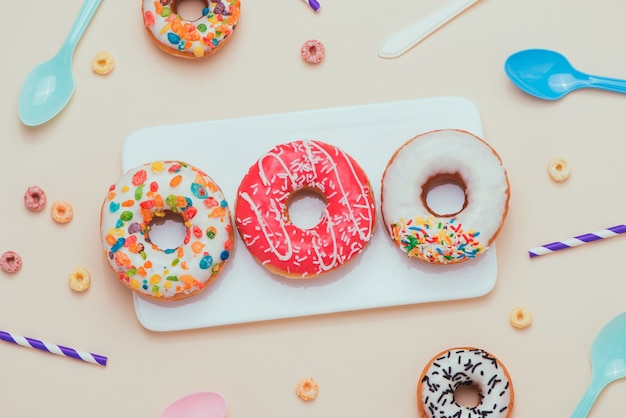 Feest. Verschillende kleurrijke suikerachtige ronde geglazuurde donuts en flessen drankjes op lichte kleur achtergrond.