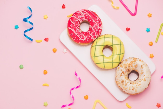 Feest. Verschillende kleurrijke suikerachtige ronde geglazuurde donuts en flessen drankjes op roze achtergrond.