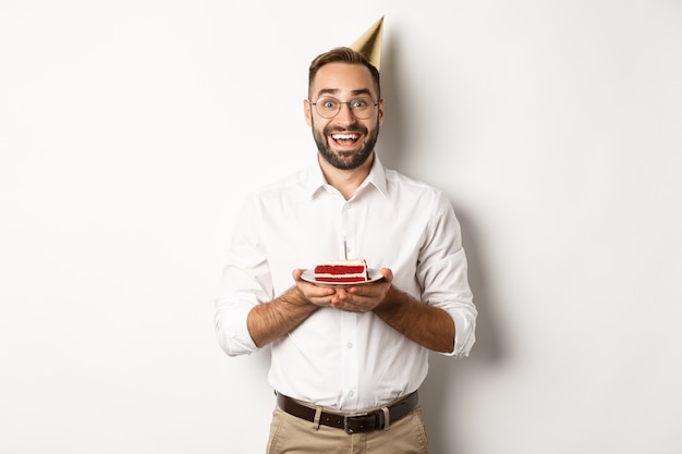 Feestdagen en feesten. gelukkig man met verjaardagsfeestje, wens maken op b-day cake en glimlachen, staande tegen een witte achtergrond.