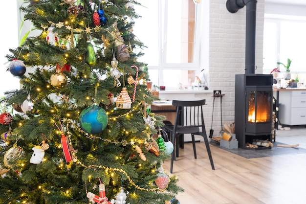 Feestelijk interieur van huis is versierd voor Kerstmis en Nieuwjaar in loft-stijl met zwarte kachel open haard kerstboom Warme studio kamer met witte keuken brandend hout gezellig en verwarming van huis