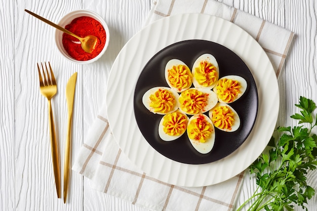 Feestelijk voorgerecht: gevulde eieren met een mix van eidooiers, sriracha saus, mayonaise, appelciderazijn bestrooid met gerookte paprika op een bord op een witte houten tafel, plat leggen, close-up