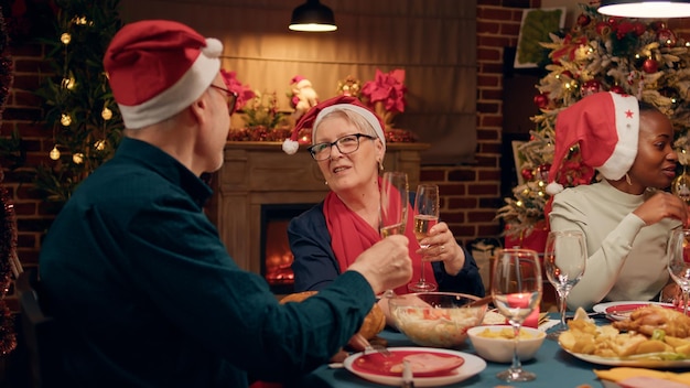 Feestelijk vrolijk senior paar rammelende glazen met champagne terwijl u thuis geniet van het kerstdiner. Gelukkige ouderen die hartelijk glimlachen tijdens het vieren van de wintervakantie.