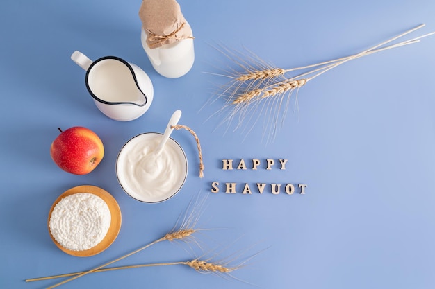 Feestelijke achtergrond voor de joodse feestdag van Shavuot zuivelproducten appel korenaren op een blauwe achtergrond met een felicitatie tekst bovenaanzicht