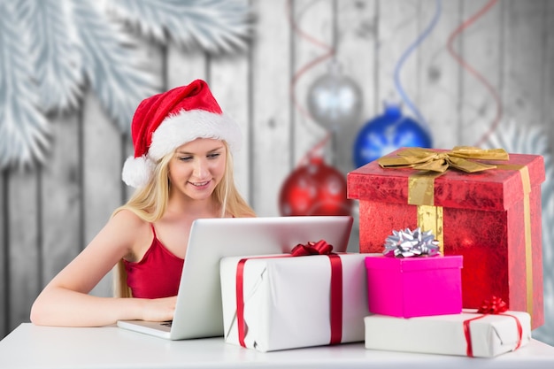 Feestelijke blonde online winkelen met laptop tegen kerstballen die over hout hangen