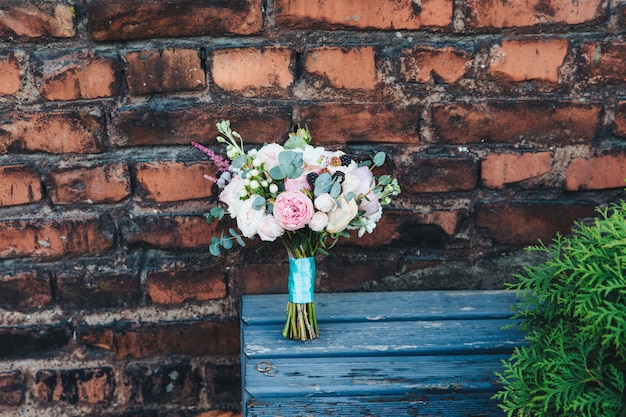 Feestelijke bruiloft bouquete vastgebonden met lint, staat op houten bank tegen verwoeste bakstenen muur