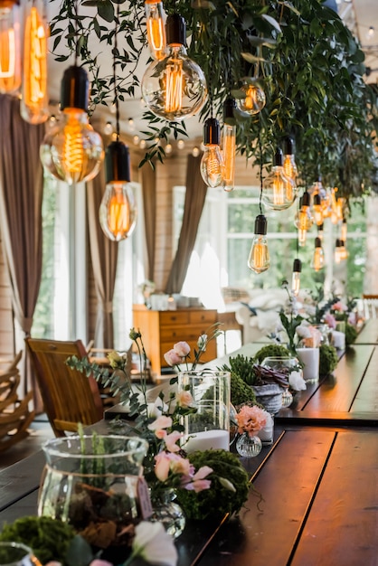 Foto feestelijke bruiloftstafel met garland of edison bollen hangend aan veters, versierd met groene bloementakken. korrelig effect