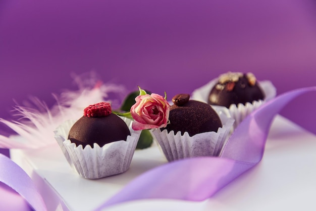 Feestelijke chocoladesnoepjes Delicate roze veren en paars lint Paars kleurenpatroon met kopieerruimte