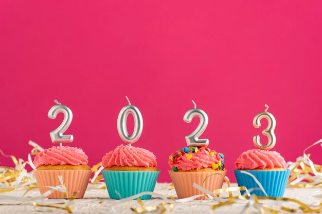 Feestelijke cupcakes en kaarsen in de vorm van nummers 2023 op roze achtergrond Concept van Nieuwjaar Kopieer ruimte