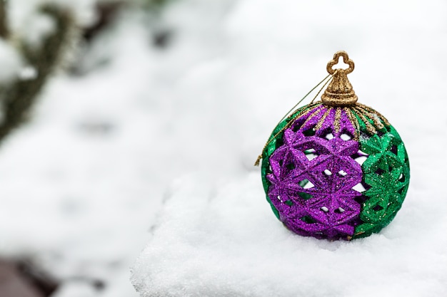 Feestelijke kerstbal gekleurd in groen en paars in de winterdag op een witte sneeuw met copyspace aan de linkerkant