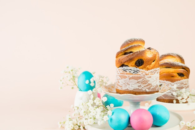 Foto feestelijke paascake met rozijnen en gekleurde eieren versierd met witte lentebloemen. horizontale foto, pastel achtergrond, kopie ruimte