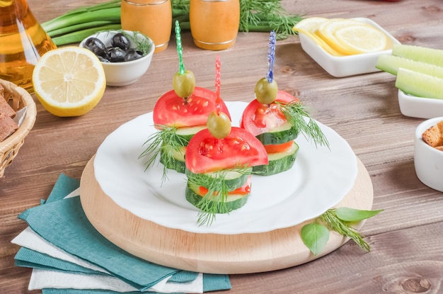 Feestelijke portie canapés met tomaten, komkommers en dille op een witte plaat op een donkere houten achtergrond.