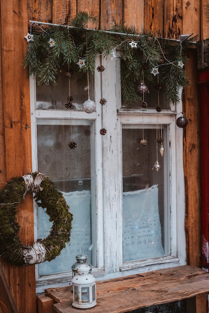 Feestelijke raamdecoratie voor nieuwjaar met dennentakken, slingers en kegels. Merry Christmas-teken en kerstballen op de vensterbank