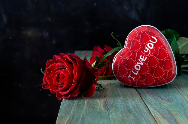 Feestelijke rode roos en een doos snoep in de vorm van een hart op houten tafel
