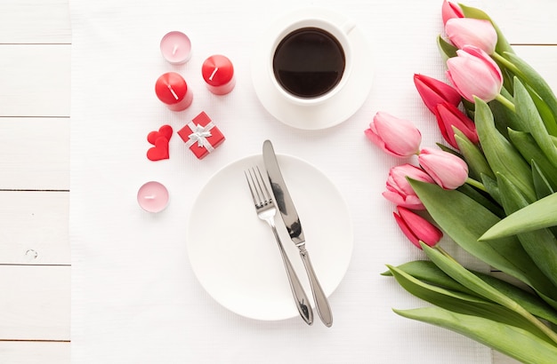 Feestelijke romantische tafelsetting met zilveren bestek en fris roze tulpenboeket.