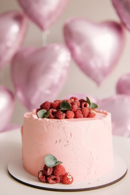 Feestelijke roze cake met frambozen op de achtergrond van heliumballonnen van roze hartjes