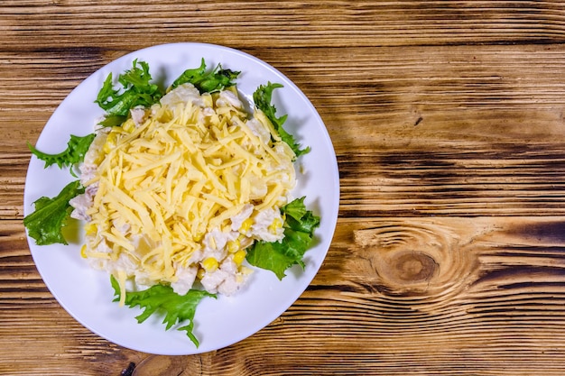 Feestelijke salade met kipfilet, ananas in blik, kaas, suikermaïs en mayonaise op rustieke houten tafel. Bovenaanzicht