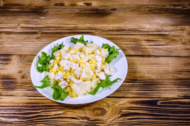 Feestelijke salade met kipfilet, ananas, kaas, zoete maïs en mayonaise op rustieke houten tafel