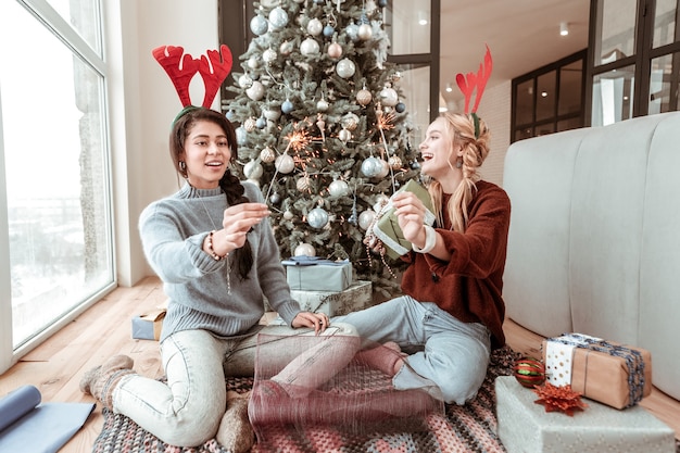 Feestelijke stemming. Gelukkig lachen langharige dames truien en spijkerbroek dragen terwijl chillen in de buurt van versierde kerstboom