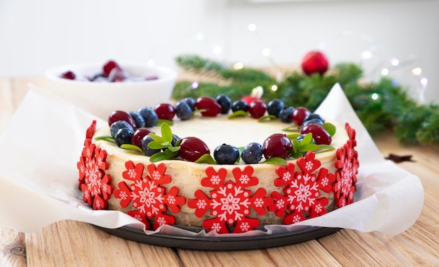 Feestelijke taart voor kerstvakantie. Cheesecake met bosbes en cranberry versierd met rode sneeuwvlokken van suikermastiek met dennentakken in bokehlichten. Lekker dessert voor de wintervakantie.