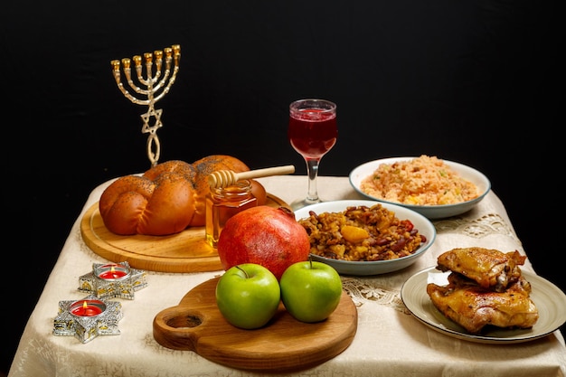 Feestelijke tafel voor een maaltijd op Rosj Hasjana challah honing granaatappel appels wijn en een traditionele chelnt naast de menora