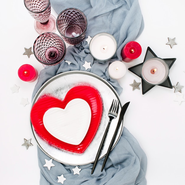 Feestelijke tafelschikking. Witte en rode gerechten in de vorm van een hart, drankglazen, kaarsen en bestek witte achtergrond. Valentijnsdag of bruiloft concept
