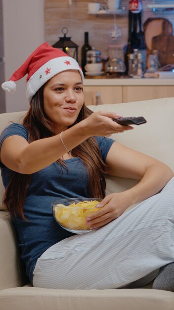 Feestelijke vrouw die een kerstmuts draagt en komedie op tv kijkt