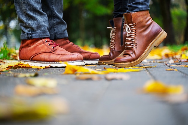 Feet of a couple in love in brown shoes on the path of the autumn park, strewn with fallen leaves. Girl stands on toes. Kiss concept
