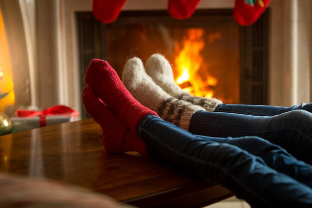 居間の燃える暖炉の近くで暖まる羊毛の靴下の家族の足