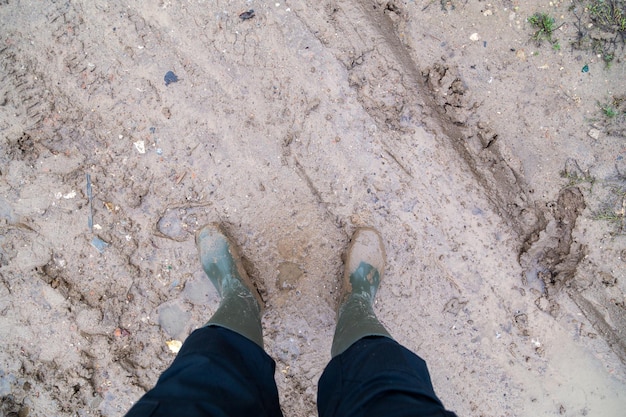 Photo feet in green rubber boots stands on wet brown mud directly above view