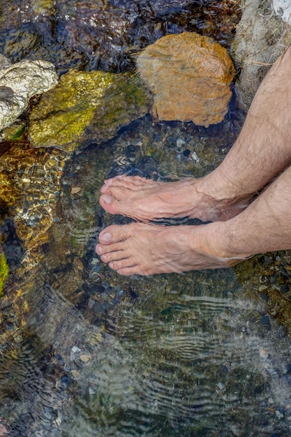 Feet immersed in the clear water with small rocks of a mountain river