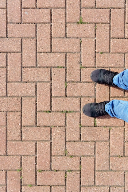 Feet in jeans and sneakers on red brick pavement