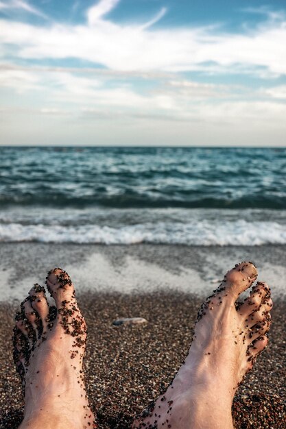 The feet of a lying man on a sandy beach near sea