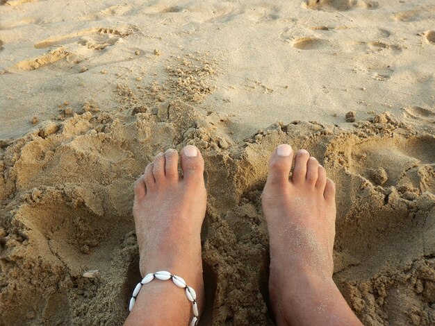 Foto i piedi di un uomo sulla spiaggia di sabbia adornati con un braccialetto alla caviglia