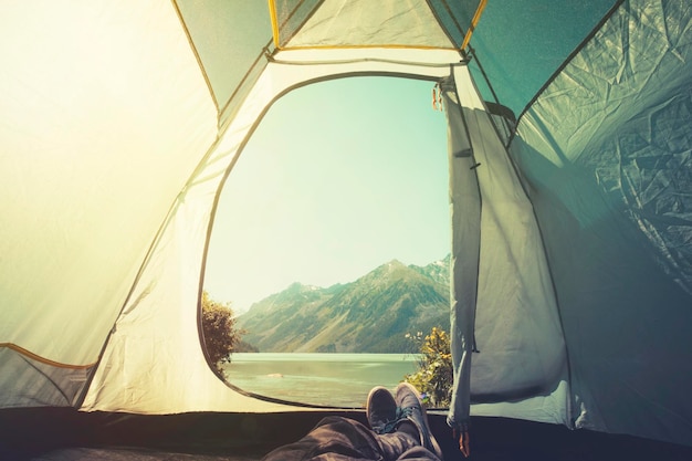 Piedi uomo che si rilassa godendo la vista delle montagne e del lago dall'ingresso del campeggio della tenda all'aperto concetto di stile di vita di viaggio vacanze estive all'aperto