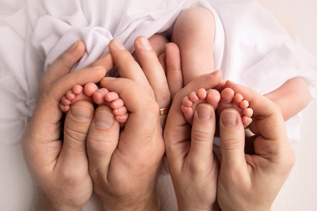 Feet of newborn twins. Two pairs of baby feet. Parents, father mother hold newborn twins by the legs. Close up - toes, heels and feet of a newborn. Newborn brothers, sisters. High quality photo