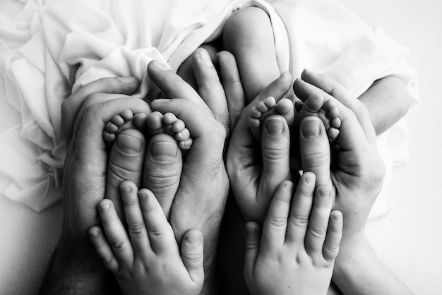 Feet of newborn twins. Two pairs of baby feet. Parents, father mother and older brother, sister hold newborn twins by the legs. Close up - toes, heels and feet of a newborn. Black and white.