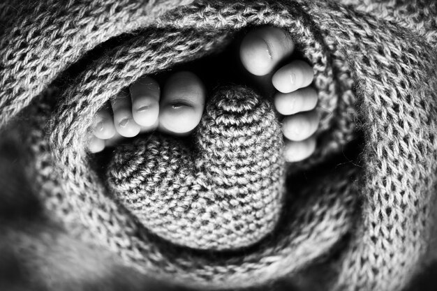 Piedi di un neonato con un cuore di legno, avvolti in una morbida coperta. fotografia in studio in bianco e nero. foto di alta qualità
