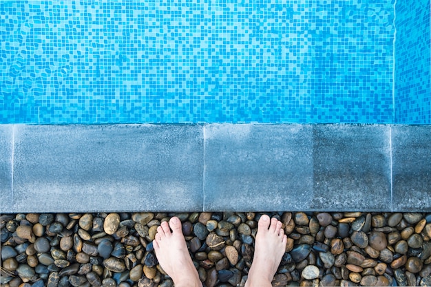 Feet at the pool side with blue mosaic tiles of swimming pool.