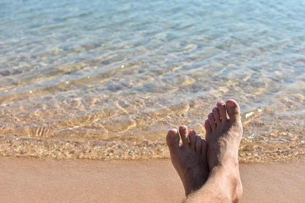 Feet in the sand on the beach against a blue sea