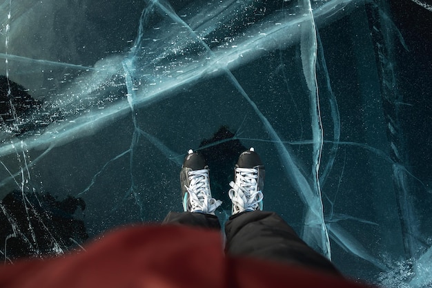 Feet in skates on the beautiful blue cracked ice of a frozen lake View of the top