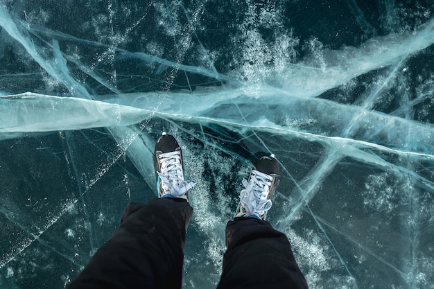 Feet in skates on the beautiful blue cracked ice of a frozen lake View of the top