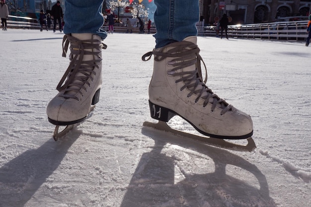 Feet in skates. Public ice-skating rink, pair of skates, scratched ice, sunny day in the winter.