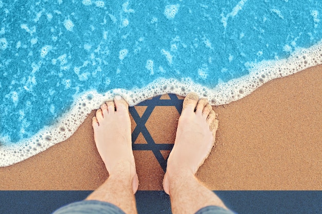 Foto piedi sulla soleggiata spiaggia sabbiosa con bandiera israele vista dall'alto sul surf