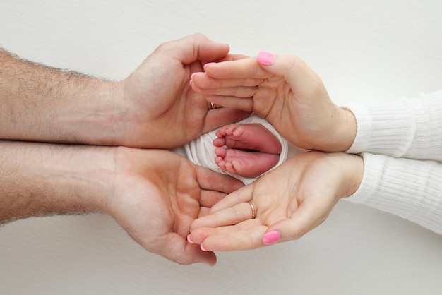 Foto piedi dita dei piedi talloni di un neonato piede dei bambini nelle mani di madre padre genitori gambe del bambino tra le braccia di mamma e papà mamma e suo figlio sfondo bianco macrofotografia primo piano