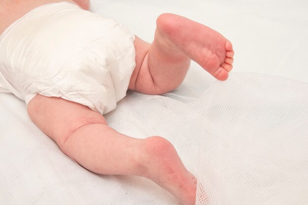 Photo feet of a two months old baby wearing diapers lying in bed at home