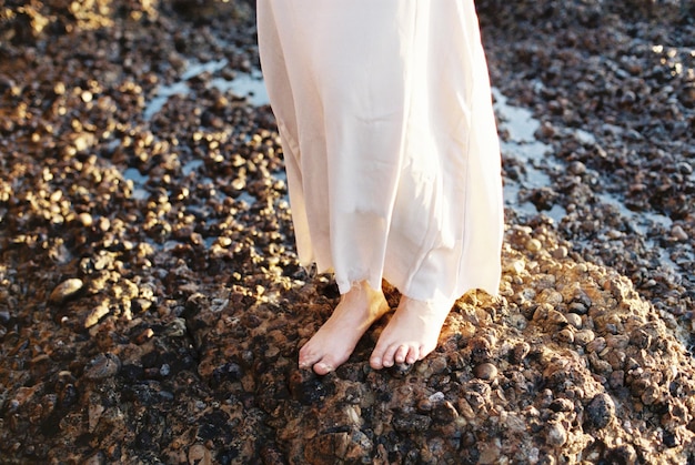 Foto i piedi di una donna in abito in piedi su una roccia