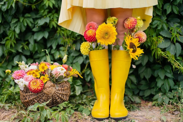 Feet in yellow rubber boots with autumn flowers near the vineyard