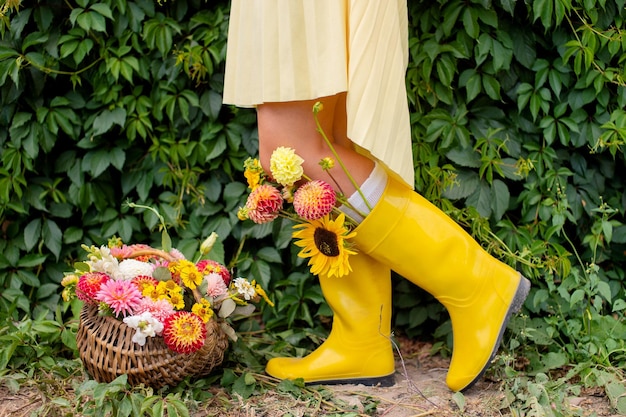 Feet in yellow rubber boots with autumn flowers near the vineyard