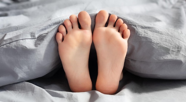 Feet of young woman lying in bed under blanket, closeup