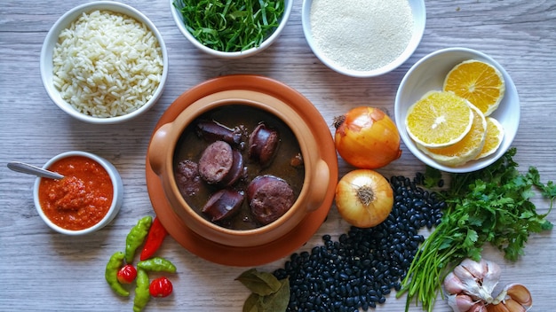 Photo feijoada in a ceramic bowl and its ingredients. brazilian food.